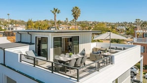 A modern rooftop terrace with a dining area, outdoor seating, and a view of the surrounding neighborhood.