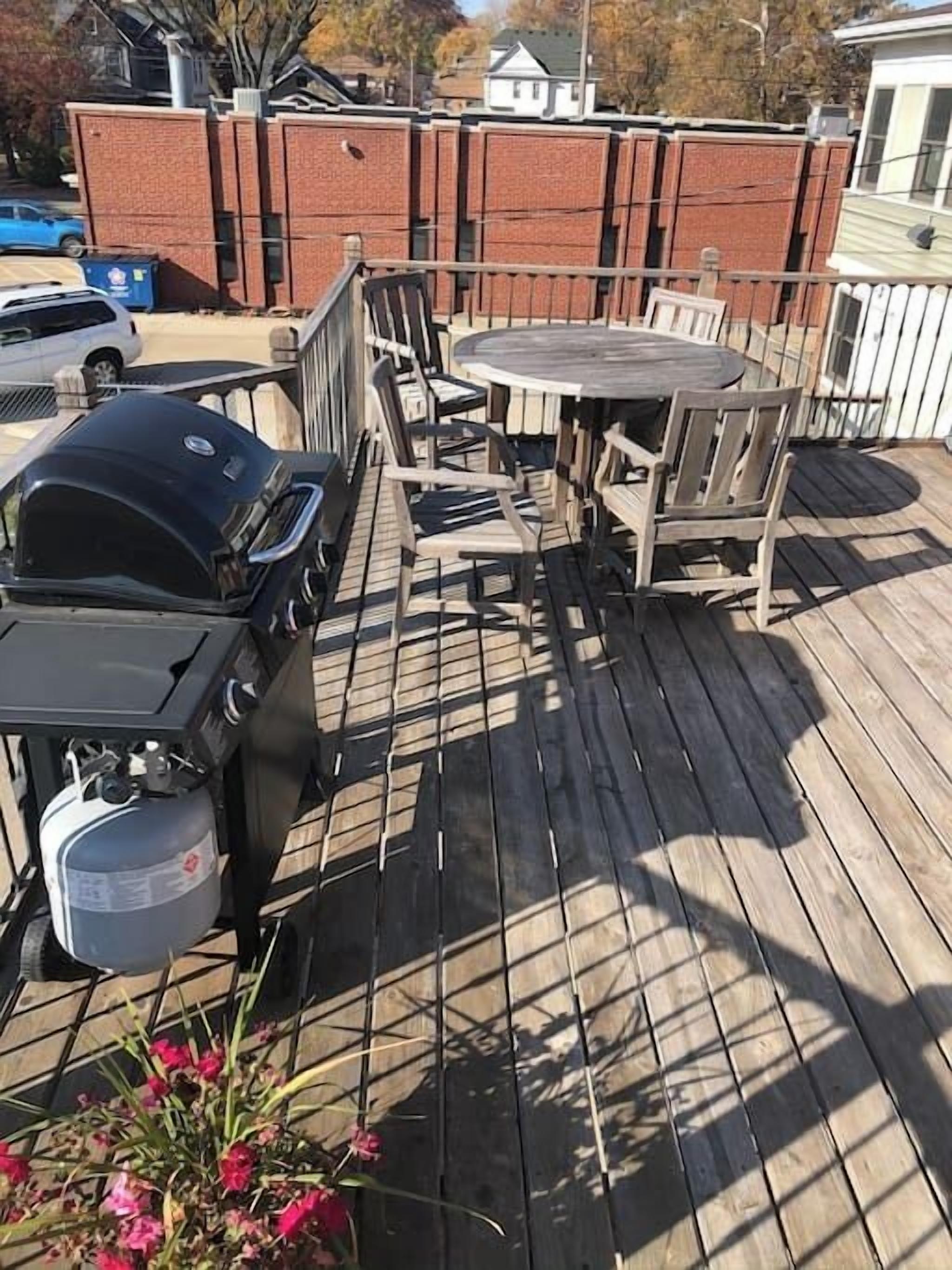 Une terrasse en bois équipée d’un barbecue, de mobilier d’extérieur et agrémentée d’un arrangement floral.