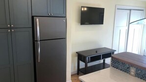 A kitchen with dark cabinets, a stainless steel refrigerator, a flat-screen TV mounted on the wall, and a wooden countertop.