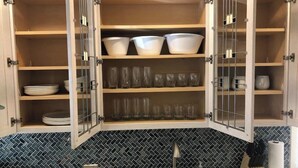 A kitchen with open cabinets displaying dishes and glasses.