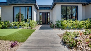 Una casa moderna con entrada pavimentada, ventanas amplias y un jardín cuidado.