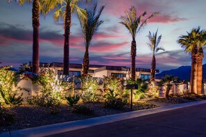 A modern building with a landscaped garden, palm trees, and a view of mountains.