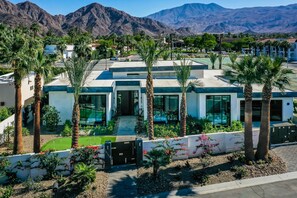 A modern hotel with a pool, palm trees, and mountains in the background.