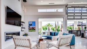 Una sala de estar moderna con un televisor grande, asientos cómodos, una mesa de centro y vistas a palmeras y montañas.