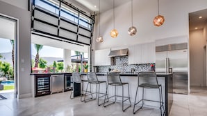 Una cocina moderna con una isla grande, taburetes de bar, electrodomésticos de acero inoxidable y vistas al exterior.