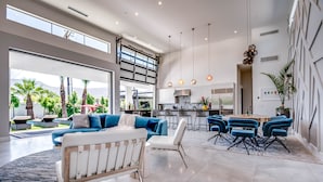 Un salón espacioso con un sofá grande, una mesa de comedor con sillas azules y una cocina al fondo.