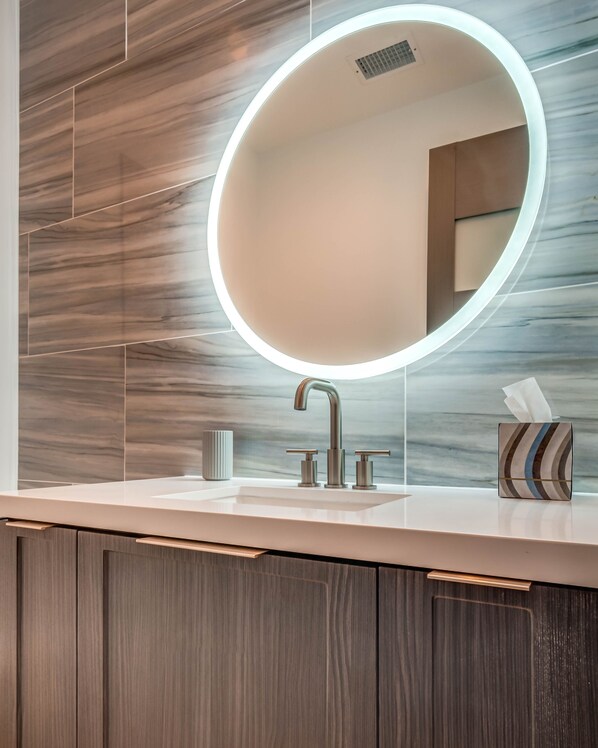 Une salle de bain moderne avec un miroir rond, un robinet et une boîte à mouchoirs sur le comptoir.