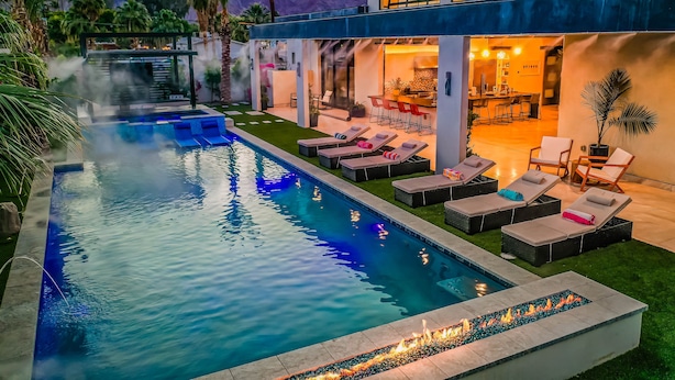 Un área de piscina moderna al aire libre con sillones reclinables, un bar y un comedor.