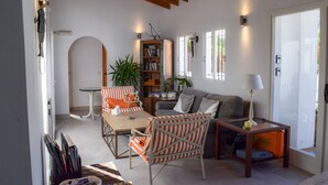 Un salon chaleureux avec un canapé, un fauteuil à rayures et une petite table sur laquelle se trouve une lampe. On y trouve également une bibliothèque remplie de livres et une plante en pot.