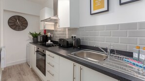 A modern kitchen with white cabinets, a black countertop, a stainless steel sink, a clock, and a framed quote on the wall. - Charnley House Apartment 2 (Blackpool)