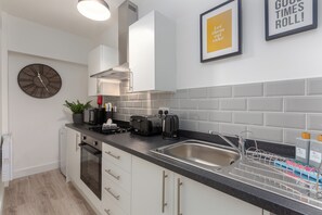 Une cuisine moderne avec des meubles blancs, un plan de travail noir, un évier en acier inoxydable, une horloge et une citation encadrée accrochée au mur.