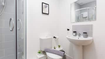 A modern bathroom with a glass shower enclosure, a white toilet, a sink with two soap dispensers, and a framed artwork on the wall.
