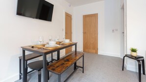 A dining area with a table set for four, a bench, a television mounted on the wall, and a small table with a plant. - Charnley House Apartment 2 (Blackpool)