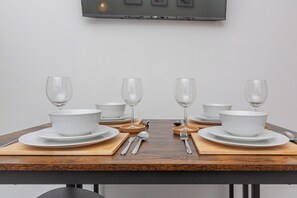 A dining table set with white dinnerware, including plates, bowls, and wine glasses, with cutlery and a wooden board.