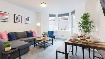 Una sala moderna con un sofá gris, un sillón azul y una mesa de comedor de madera dispuesta para una comida.