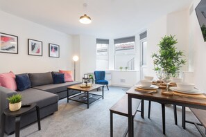 A modern living room with a grey sofa, blue armchair, and a wooden dining table set for a meal.