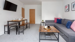 A modern living room with a grey sofa, wooden coffee table, and a TV mounted on the wall. - Charnley House Apartment 2 (Blackpool)