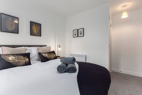 A neatly made bed with rolled towels, a black and white headboard, and decorative pillows.
