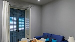 A compact living space with a blue sofa, a wooden table, and a small side table with a lamp. - Superior Suite (Trapani)