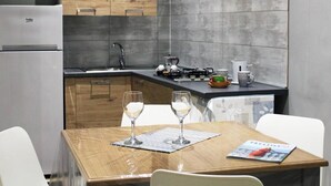 A modern kitchen with a refrigerator, stove, and sink. There is a dining table with two wine glasses and a magazine. - Superior Suite (Trapani)