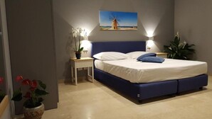 A bedroom with a bed, bedside tables, and a wall-mounted painting. - Deluxe Suite (Trapani)