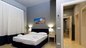 Habitación de hotel con cama, dos mesitas de noche, un cuadro en la pared y vista al pasillo.