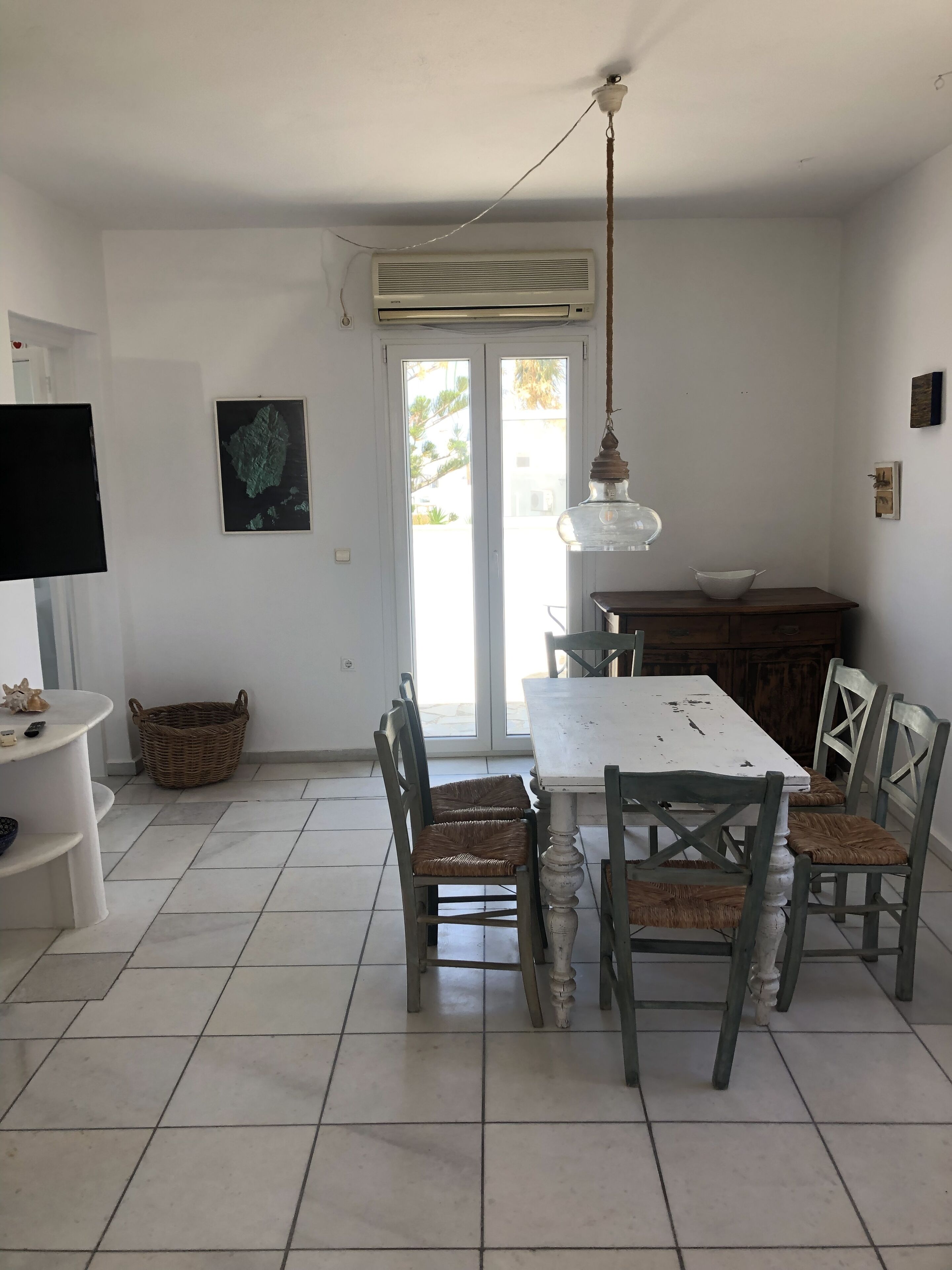 Zona pranzo con tavolo bianco, sedie in vimini e lampadario.