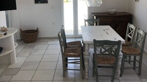 Un coin repas avec une table blanche, des chaises en osier et un luminaire suspendu.