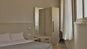Een moderne hotelkamer met een bed, een kledingkast, een nachtkastje en een raam met gordijnen.
