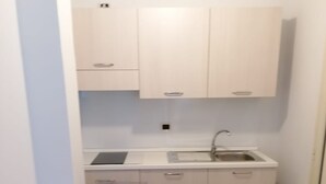 Een kleine keuken met witte kasten, een spoelbak en een aanrecht. Er staat een tafel met een stoel en een kleine kom op.