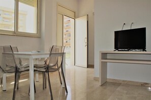 Ein modernes Zimmer mit einem Esstisch und Stühlen, einem Fernseher auf einem Schrank und einer Tür, die zu einem Balkon führt.