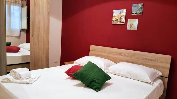 A neatly made bed with white and red pillows, a wooden headboard, and a red wall with three small pictures.