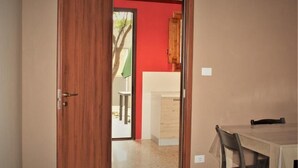 Une porte en bois ouverte donne sur une pièce dont un mur est rouge et qui contient une petite table avec une chaise.