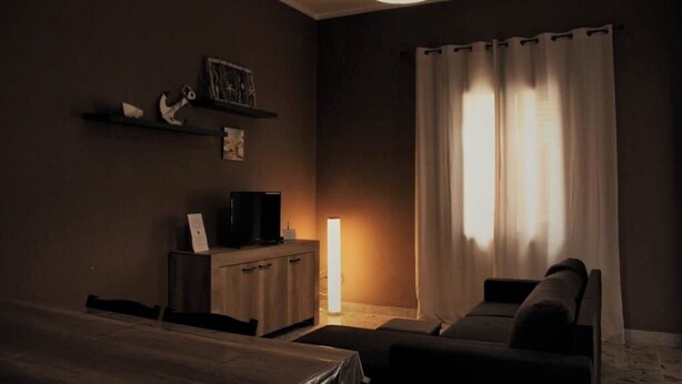 Une pièce faiblement éclairée, avec un lit simple, une table de chevet, un téléviseur et une lampe.