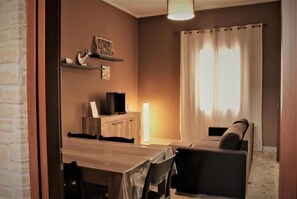 A cozy living room with a wooden table, a sofa, and a TV on a wooden cabinet.