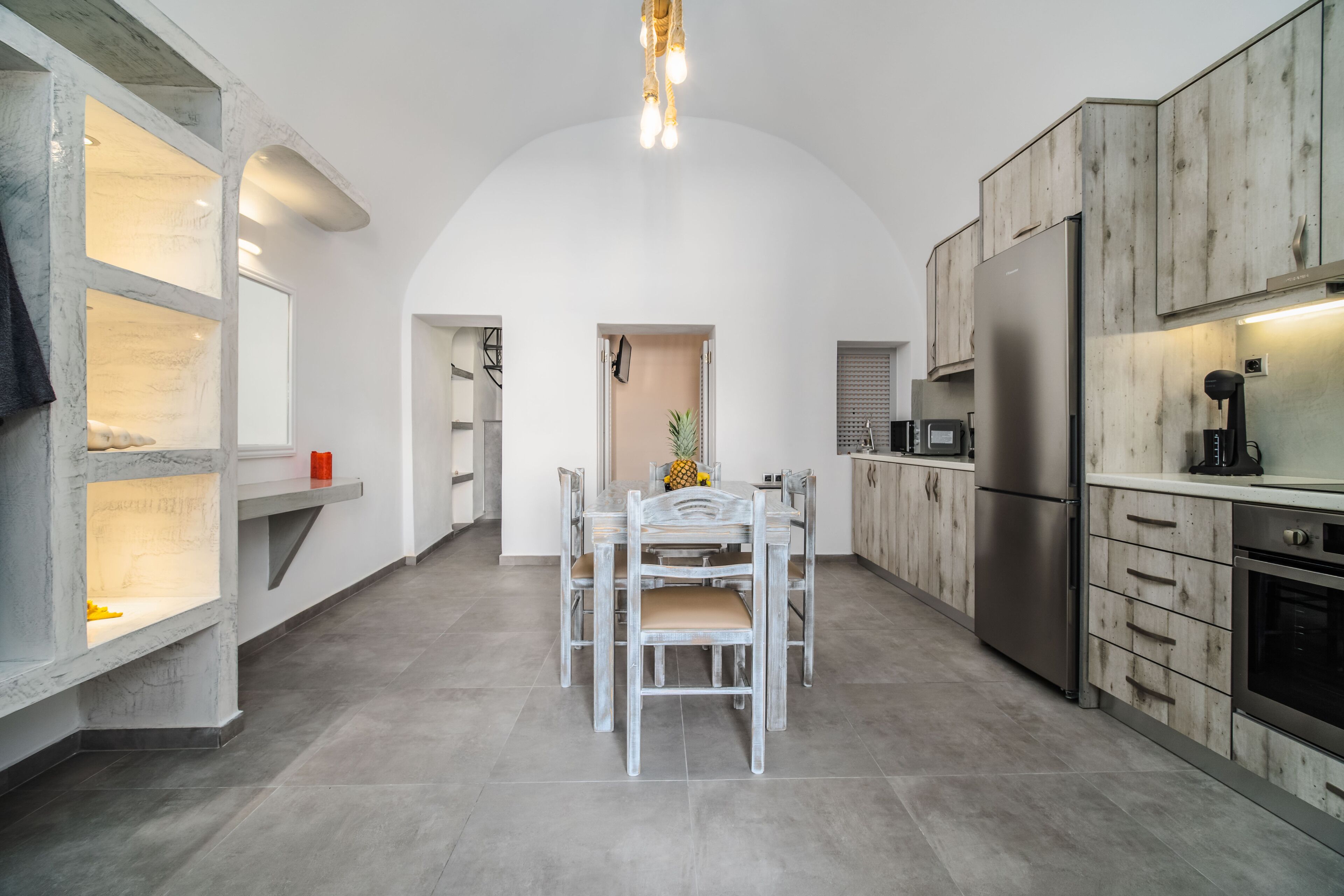 Une cuisine moderne avec un coin repas, comprenant un îlot central, des appareils électroménagers intégrés et une grande porte cintrée.