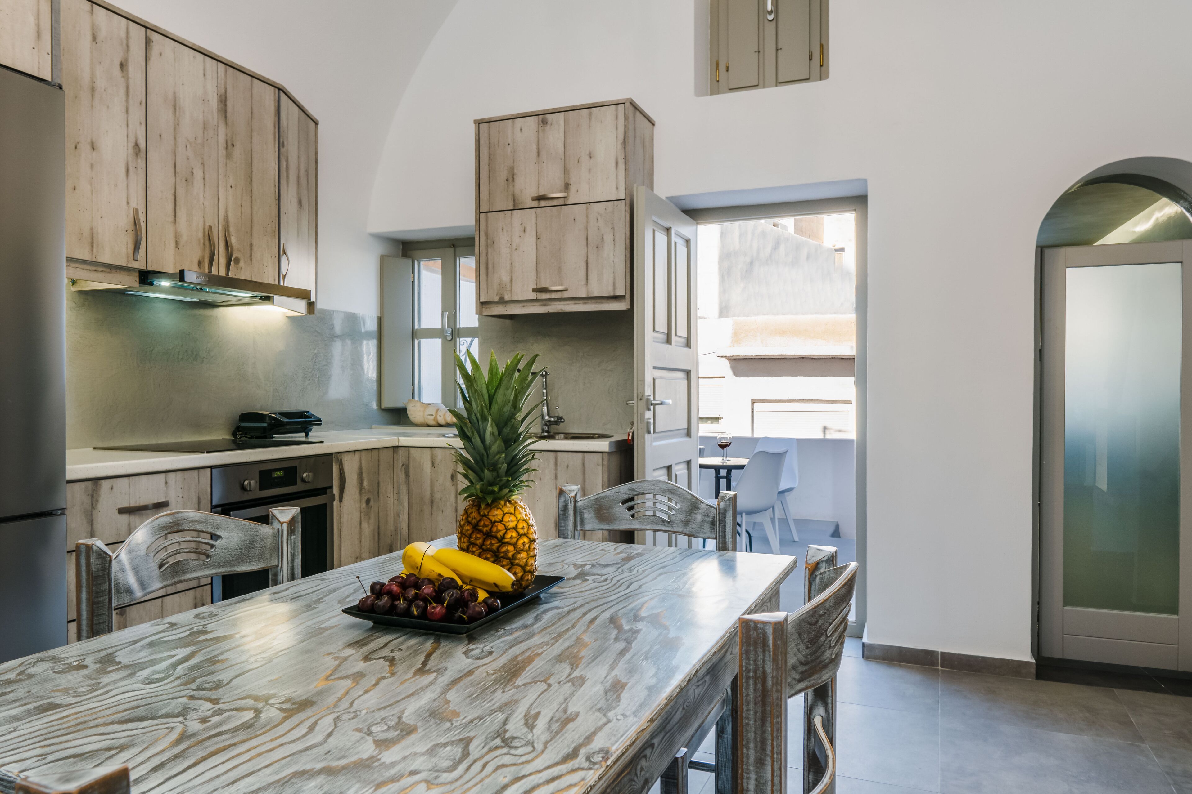 A modern kitchen with wooden cabinets, a marble countertop, and a dining area with chairs.