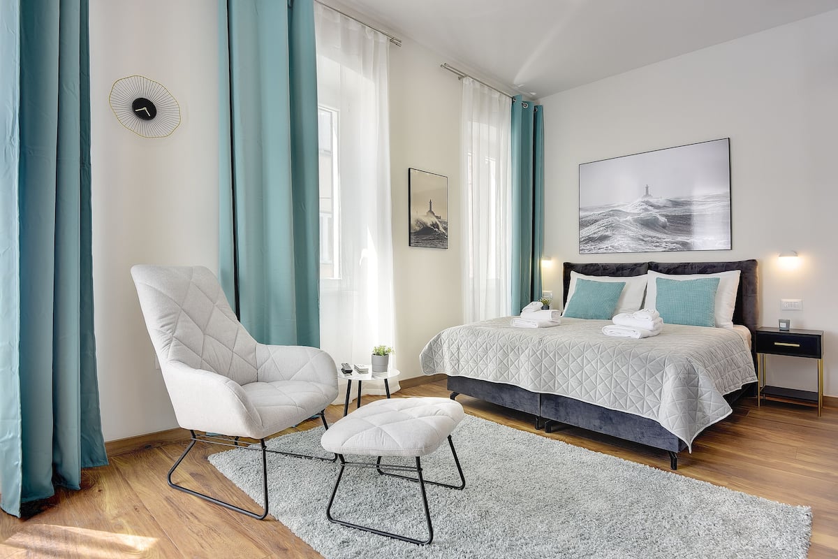 A modern bedroom with a bed, a chair, a small table, and a wall clock.