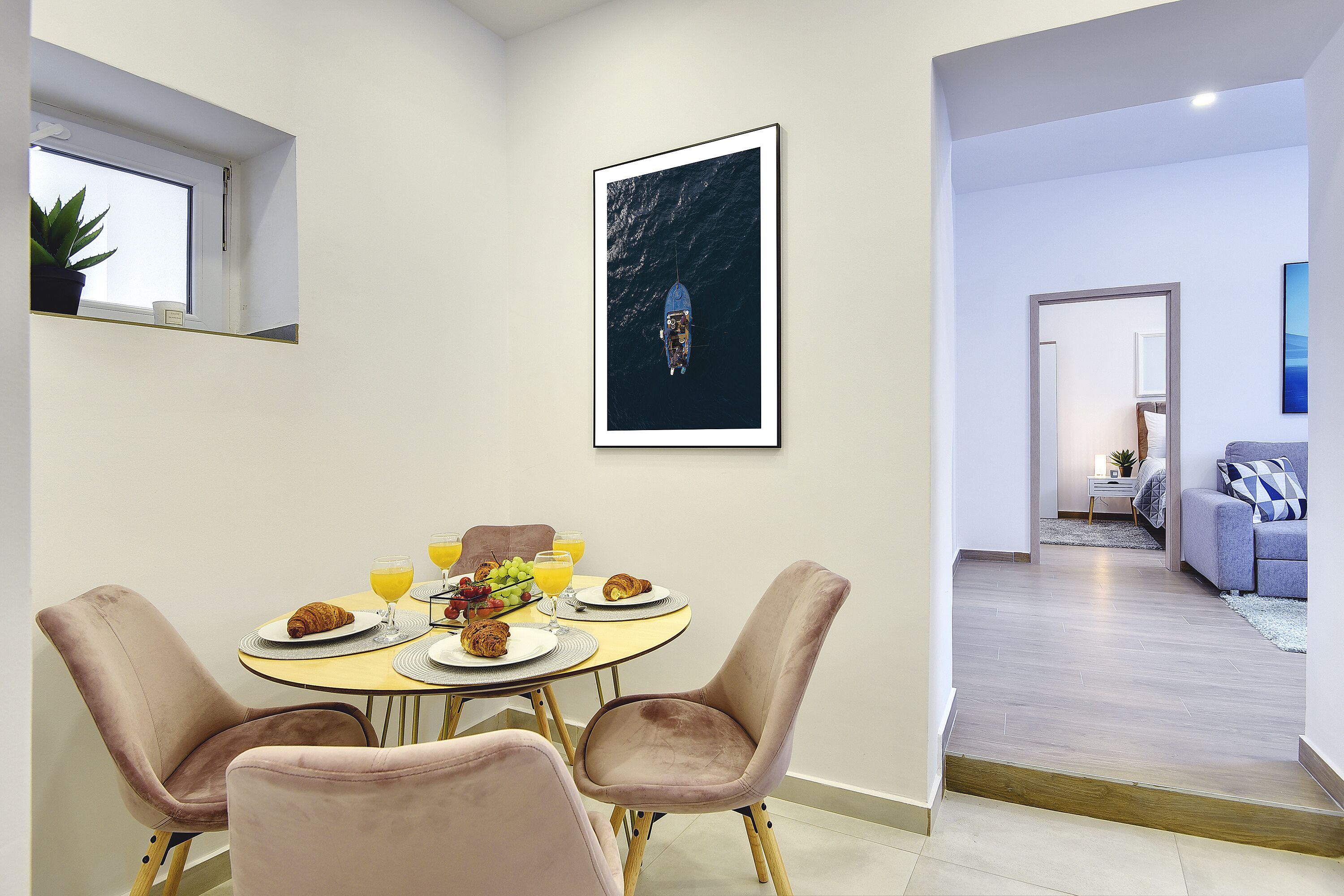 A dining area with a round table, four chairs, and a framed artwork on the wall.