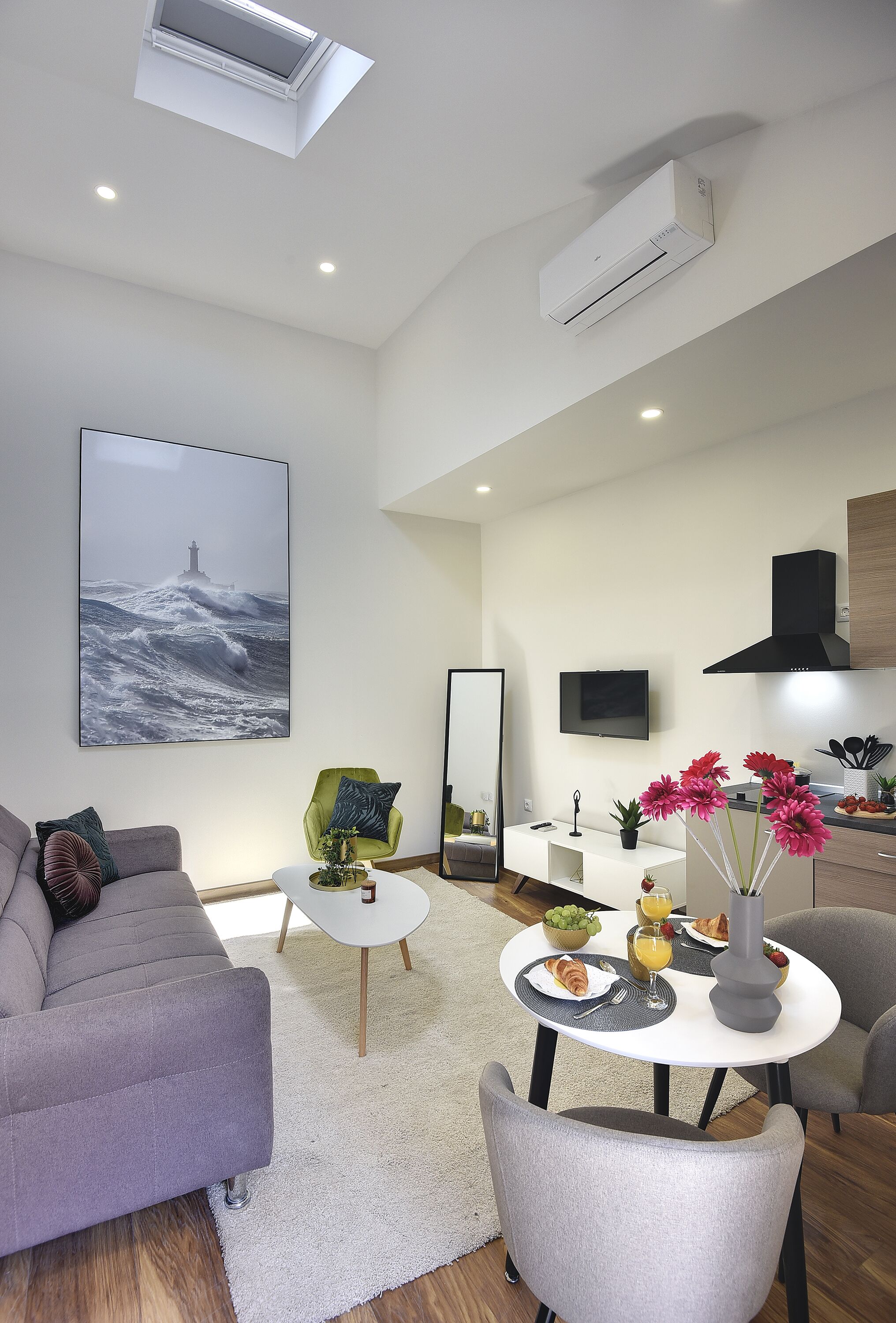 A modern living room with a grey sofa, a white coffee table, and a dining area with a white table set for breakfast.