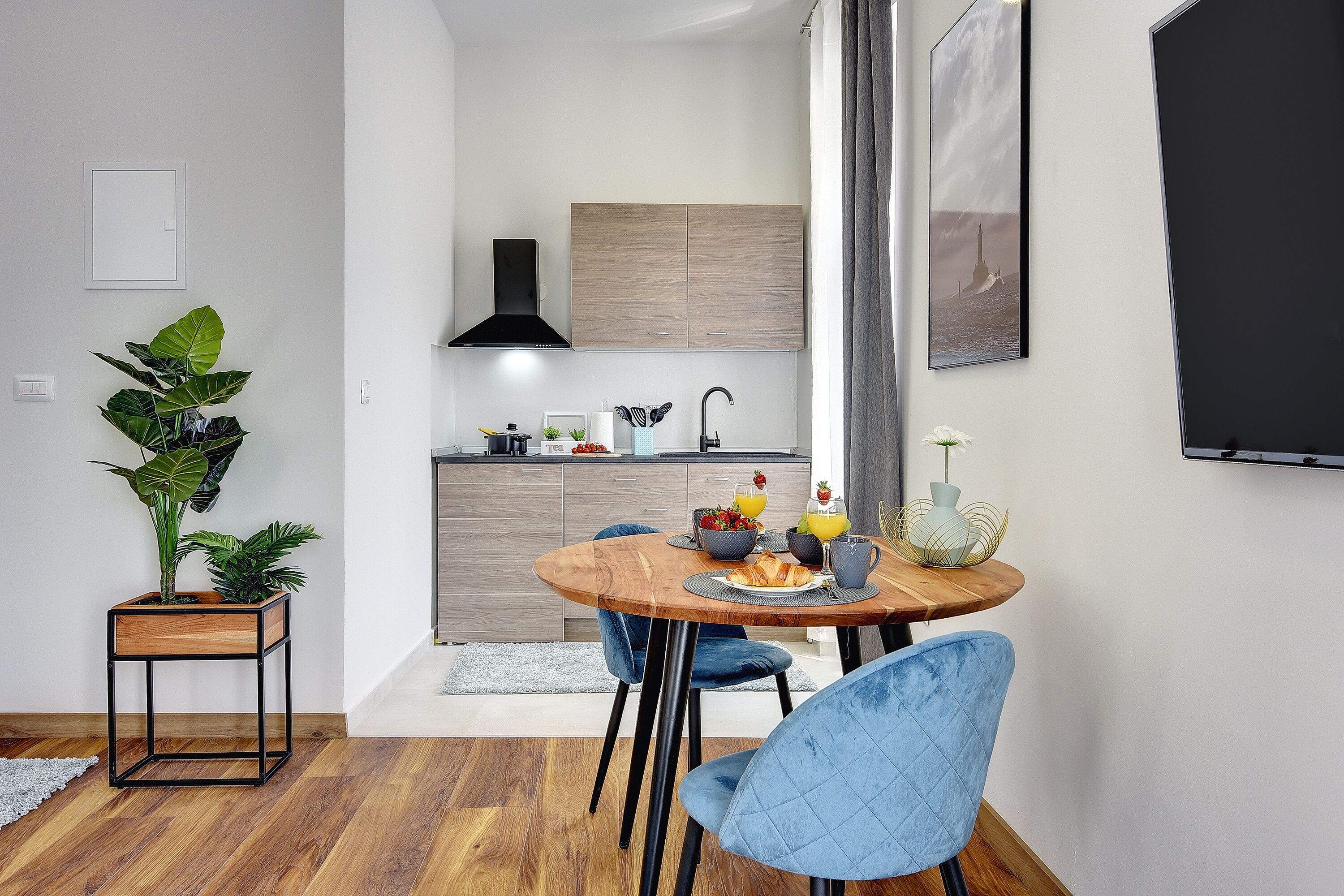 Une cuisine moderne avec des meubles en bois, une hotte noire et un coin repas comprenant une table en bois et des chaises bleues.