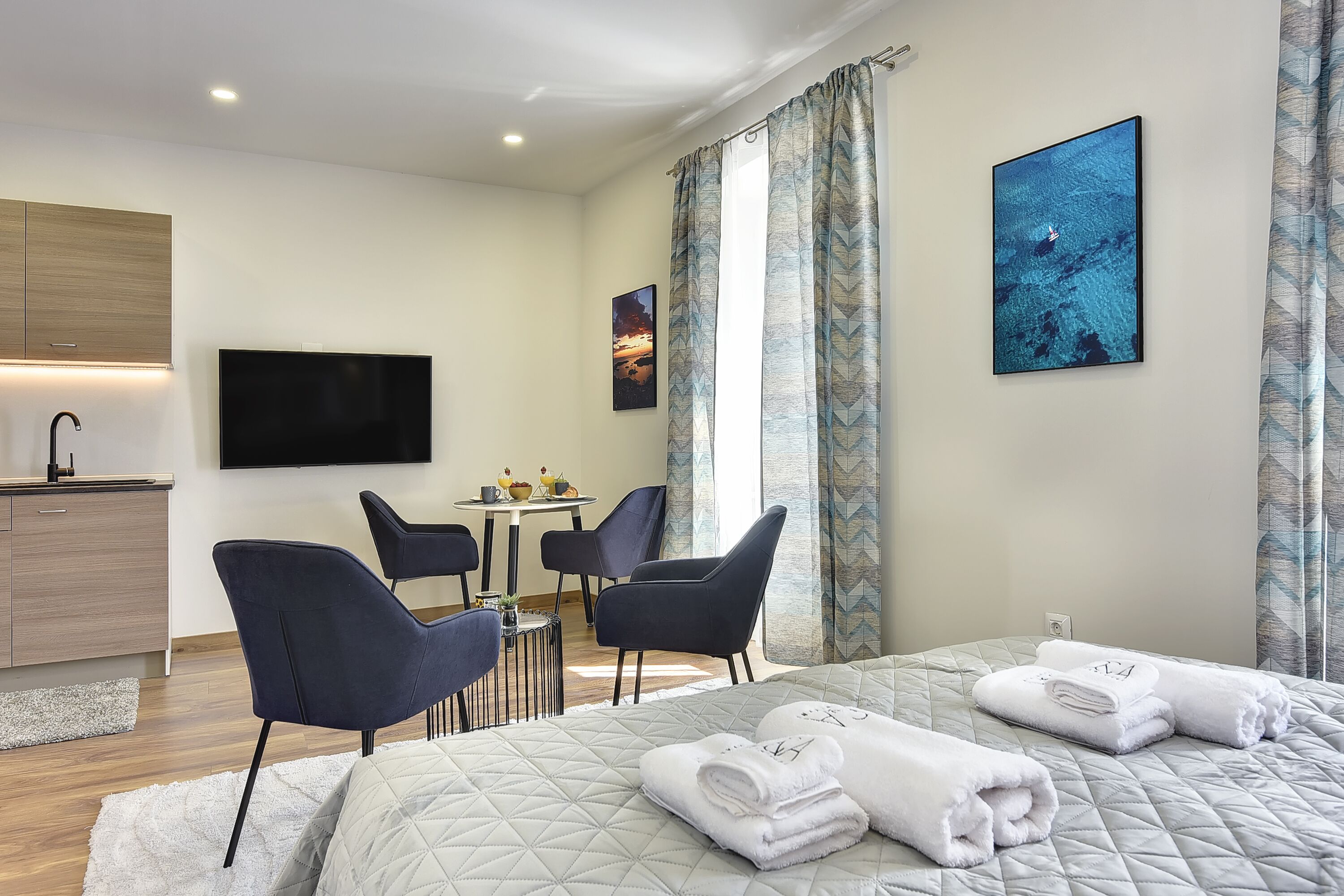 Una habitación de hotel moderna con una cama, dos sillas, una mesita, un televisor y obras de arte en las paredes.