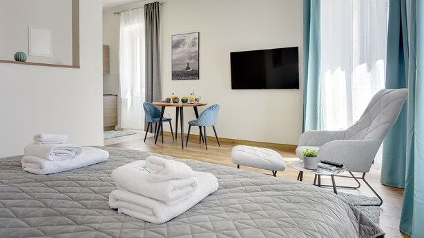Una habitación de hotel con cama, escritorio, sillas, televisión y ventana con cortinas.