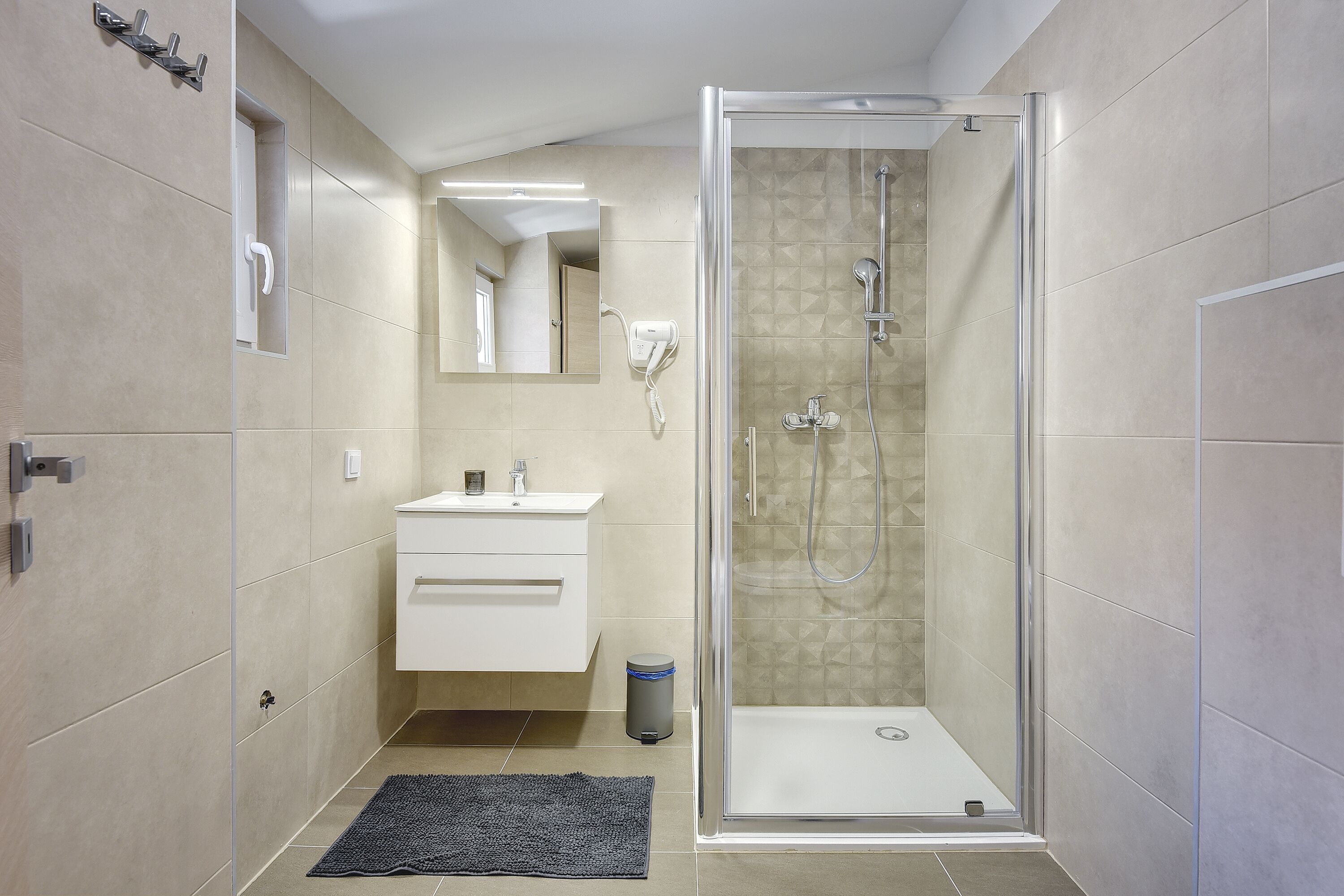 Un baño moderno con ducha de vidrio, tocador con espejo y una alfombra pequeña en el suelo.