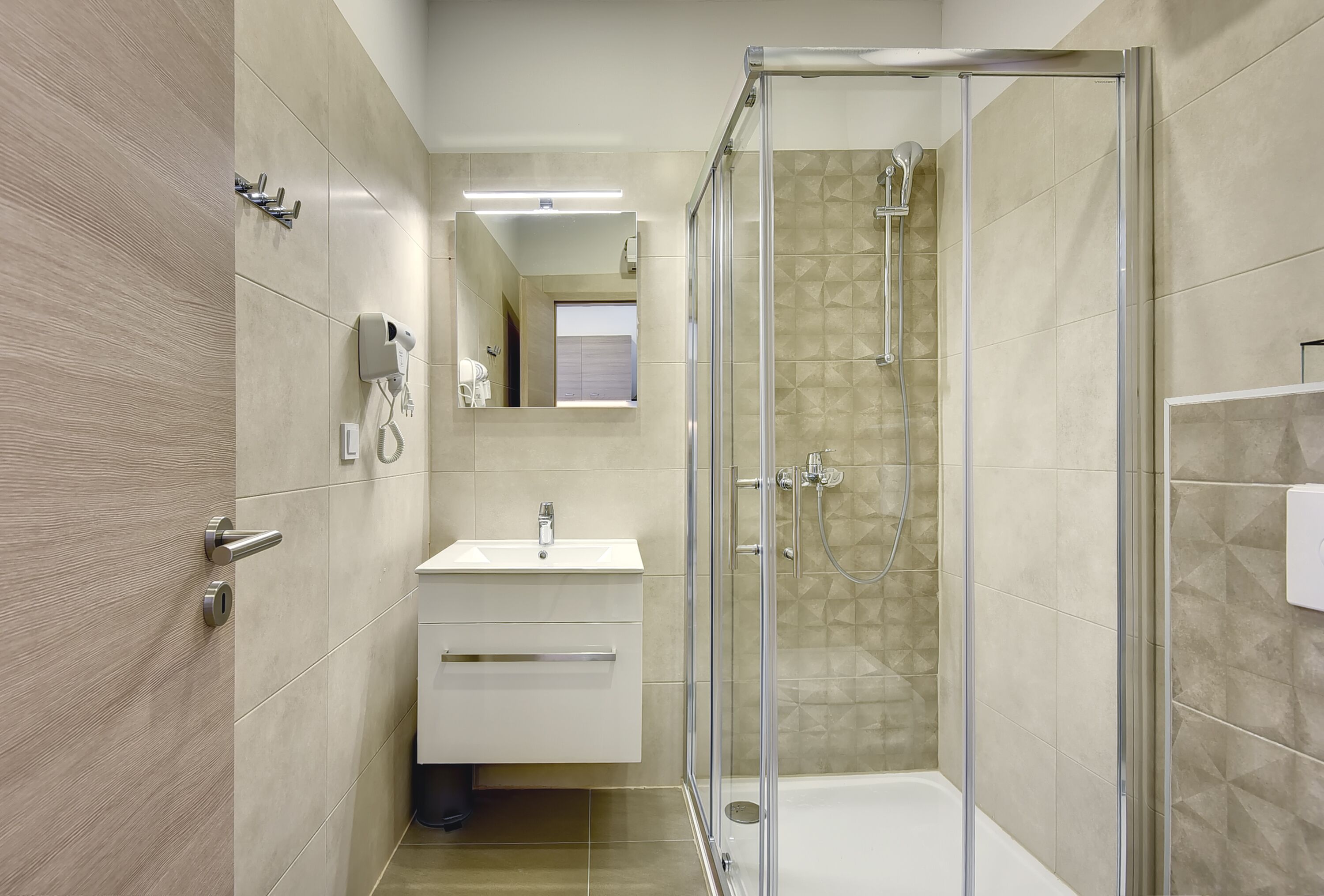 A modern bathroom with a glass-enclosed shower, a white sink, and a mirror above the sink.