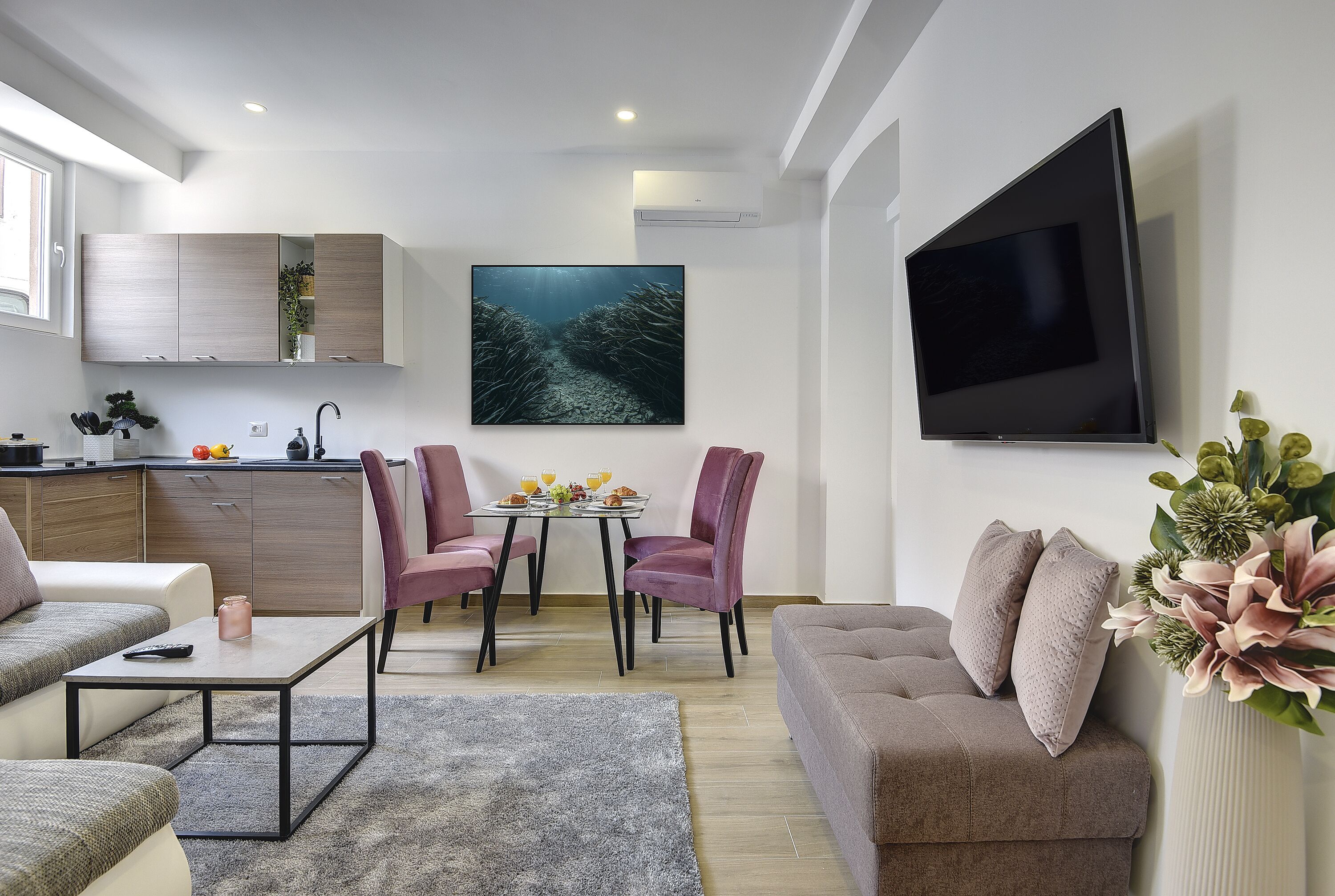 Ein modernes Wohnzimmer mit Essbereich, einem an der Wand montierten Flachbildfernseher und einem großen Fenster, das für natürliches Licht sorgt.