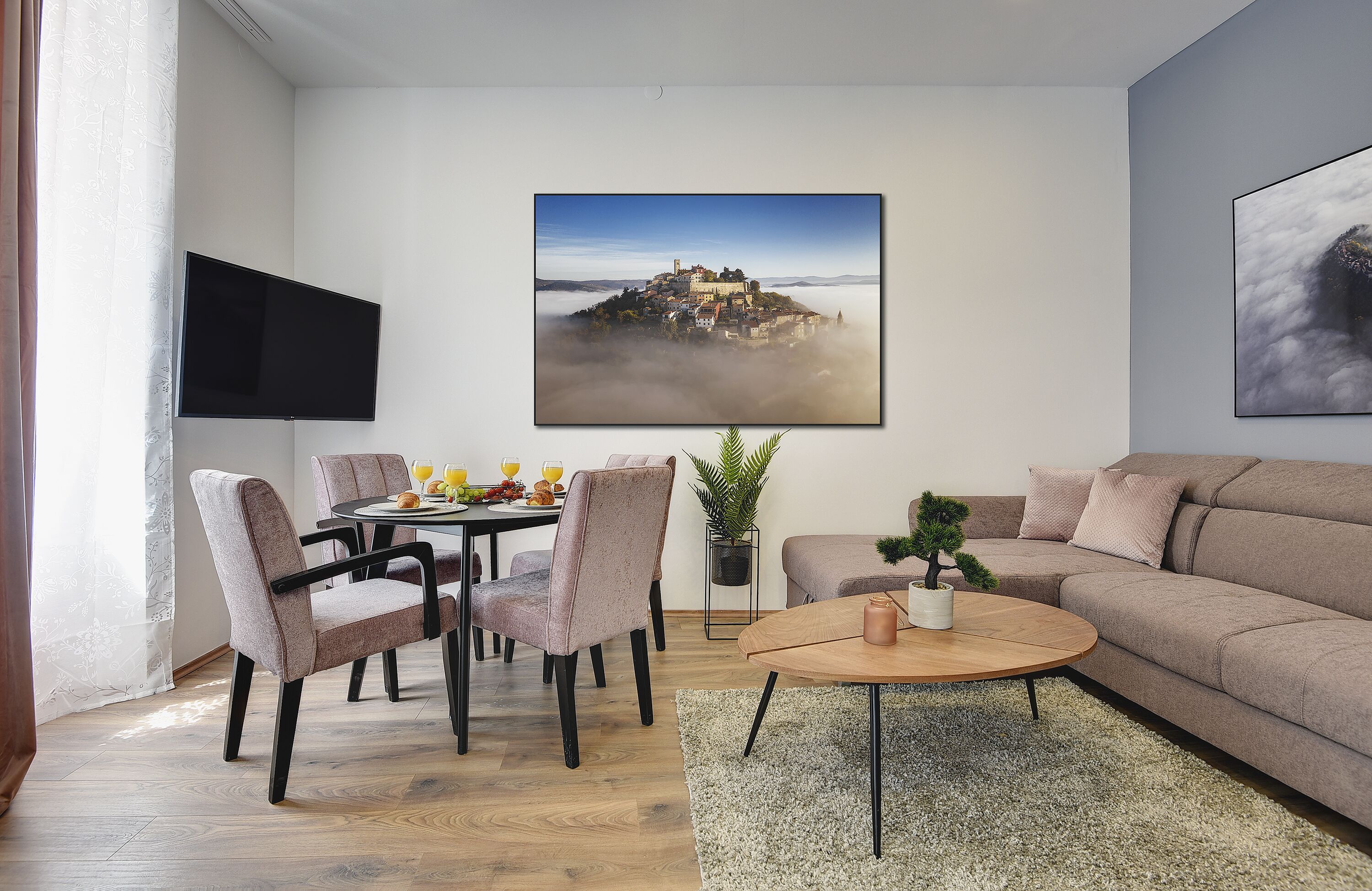 Uma sala de estar moderna com área de jantar, televisão de tela plana na parede e uma grande imagem emoldurada de uma paisagem montanhosa.