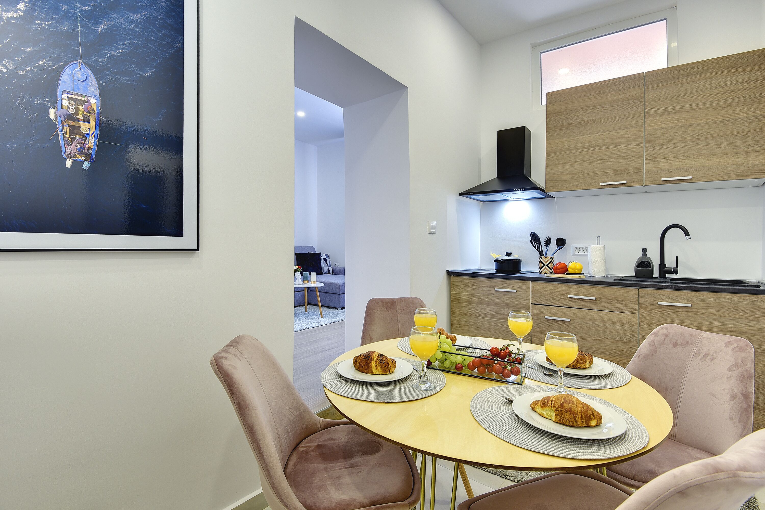 A modern kitchen with wooden cabinets, a dining area with a round table, and a large window overlooking the sea.