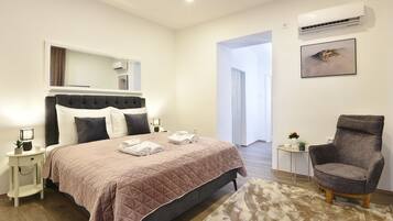 A bedroom with a bed, bedside tables, a chair, a rug, a mirror, an air conditioner, and a framed picture on the wall.