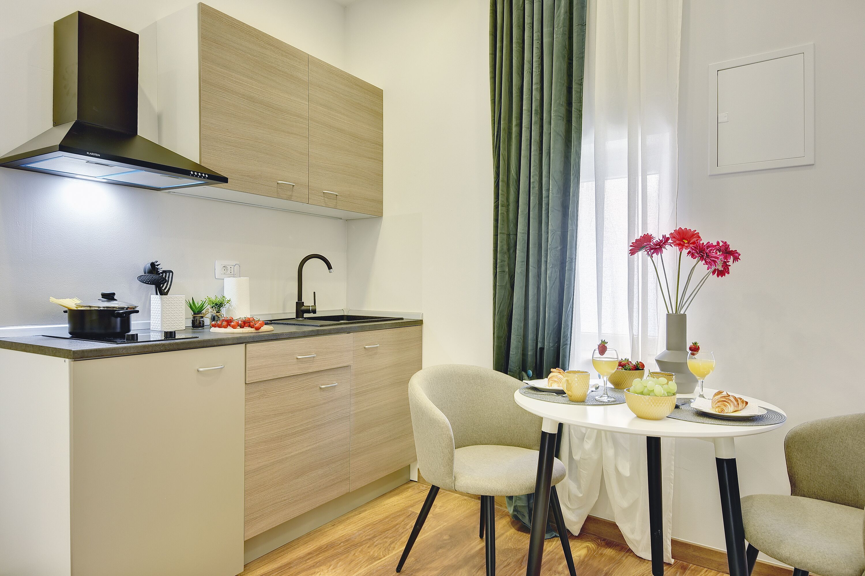 Una cocina moderna con estufa, pileta y armarios de madera. Hay una mesa de comedor con sillas y un florero con flores.